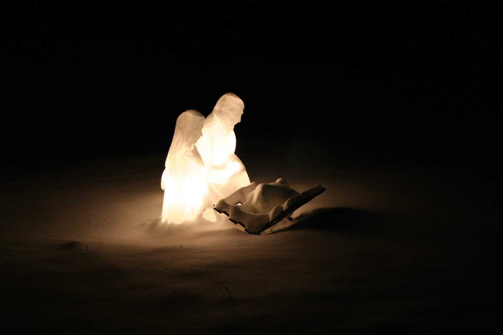White illuminated nativity set in the snow after dark