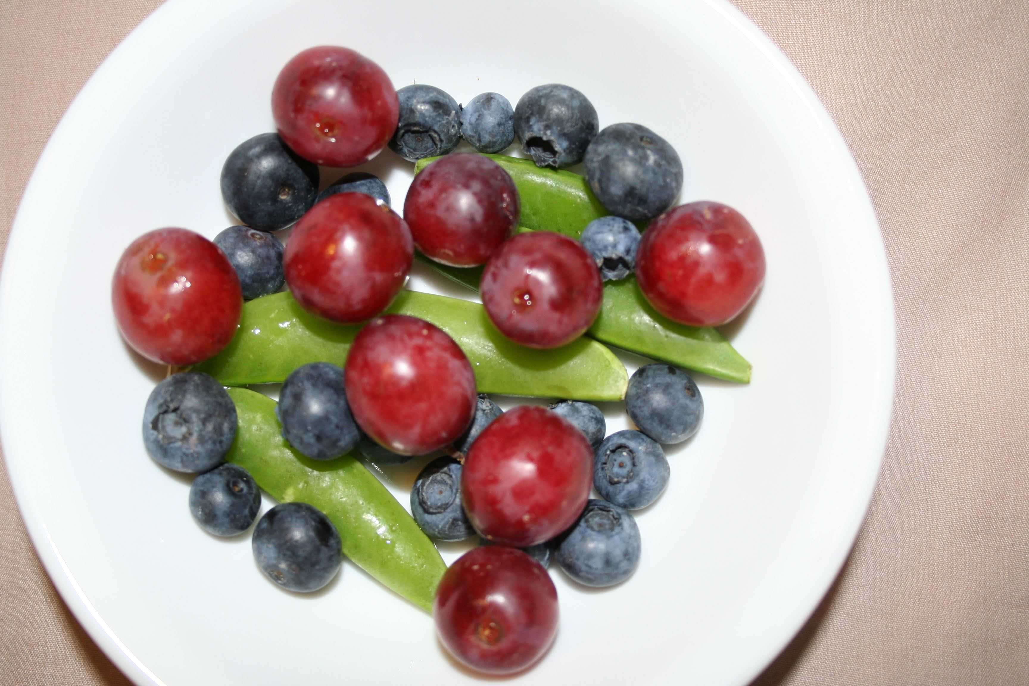 A white bowl of grapes, blueberries, and sugar snap peas